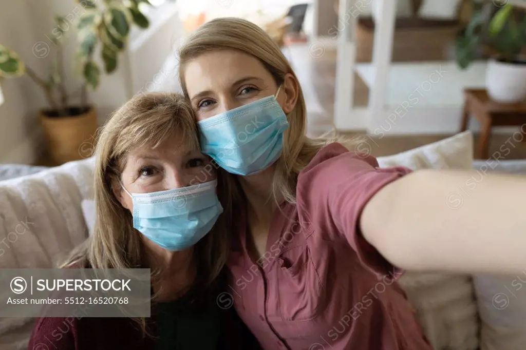 Senior Caucasian woman spending time at home with adult daughter,sitting on couch talking and using smartphone, taking selfie. Social distancingduring Covid 19 Coronavirus quarantine