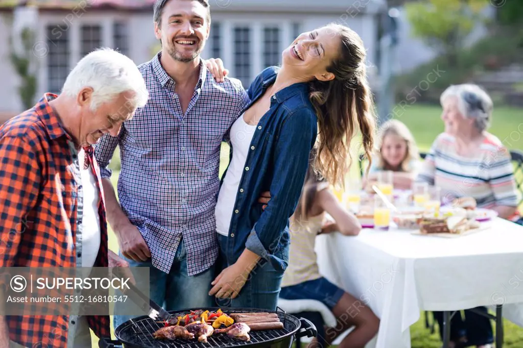 Couple and a senior man at barbecue grill preparing a barbecue in garden