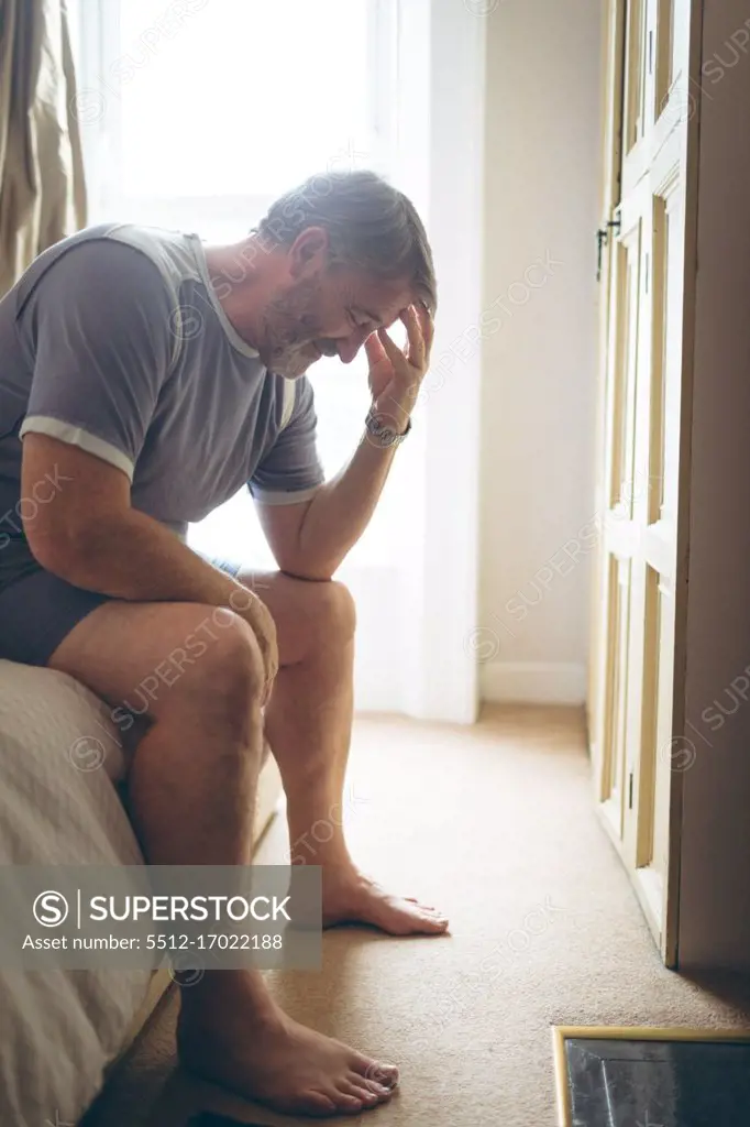 Tensed senior man sitting on bed in bedroom at home