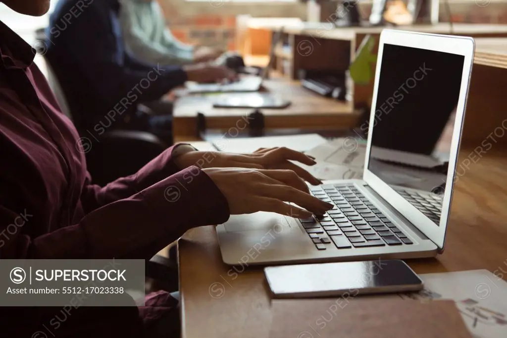 Mid section of executive using laptop at desk in office