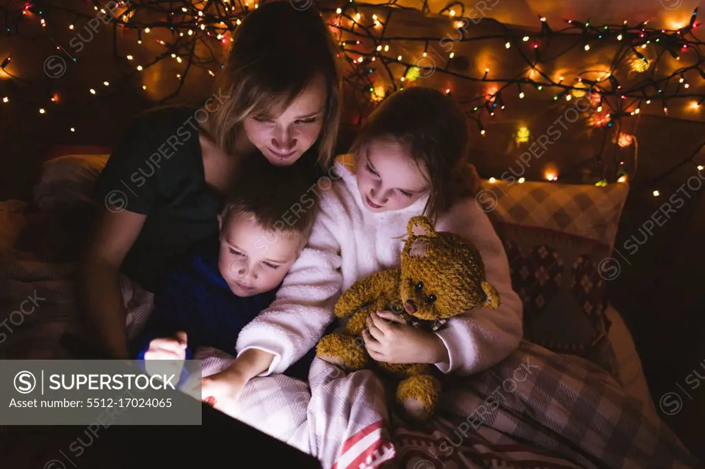 Mother and kids using digital tablet on bed against Christmas decoration