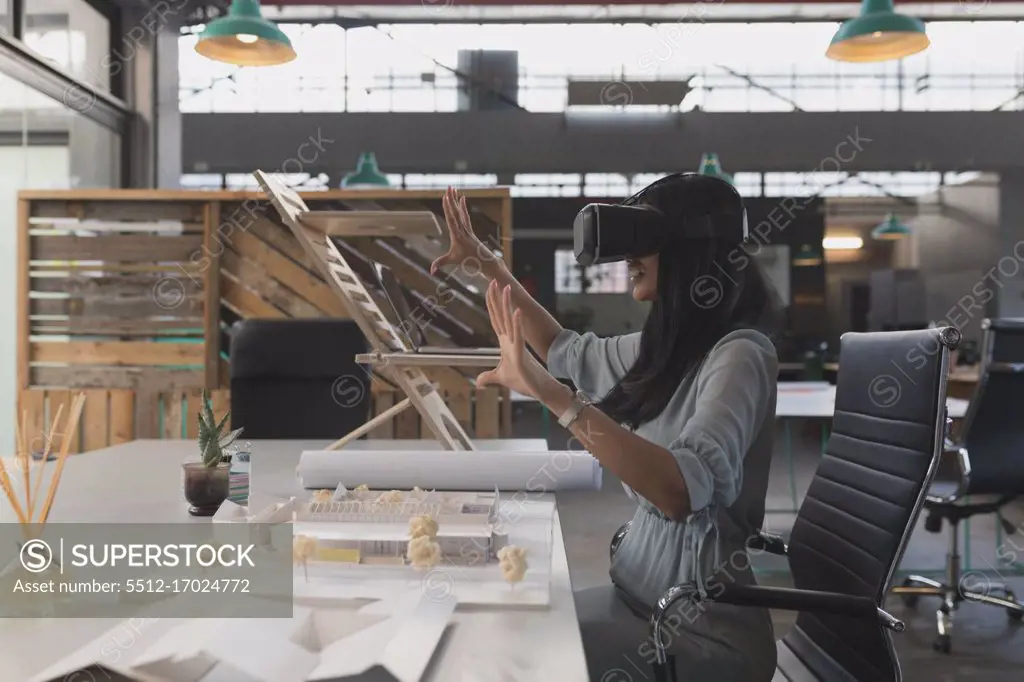 Female executive using virtual reality headset at table in office