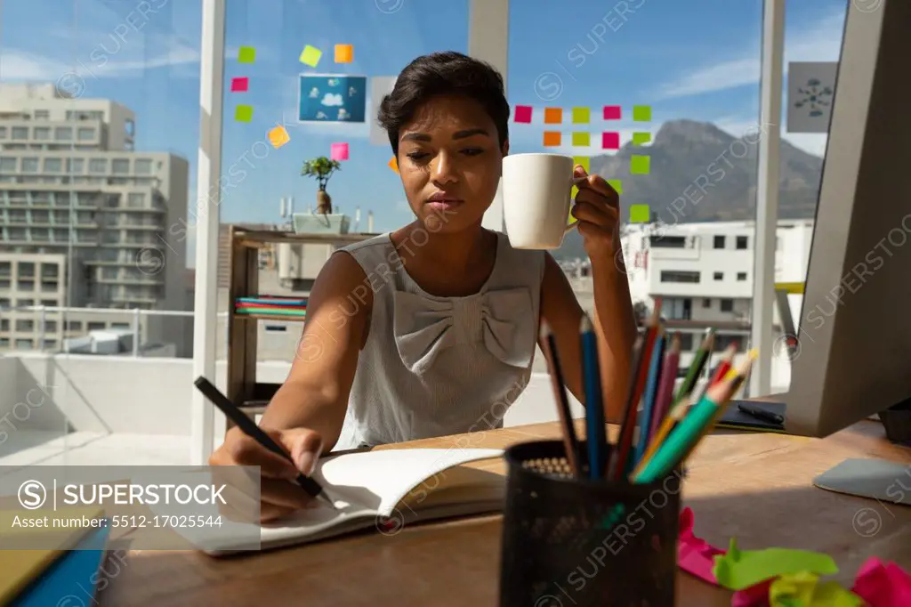 Business executive having coffee while writing on diary in office