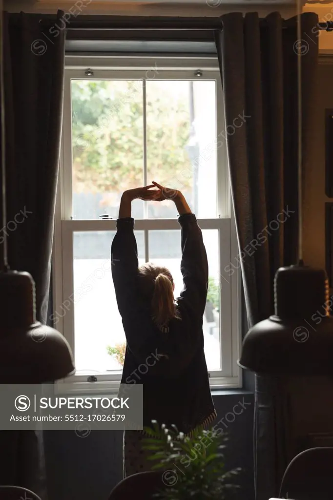 Rear view of woman standing with arms up at home