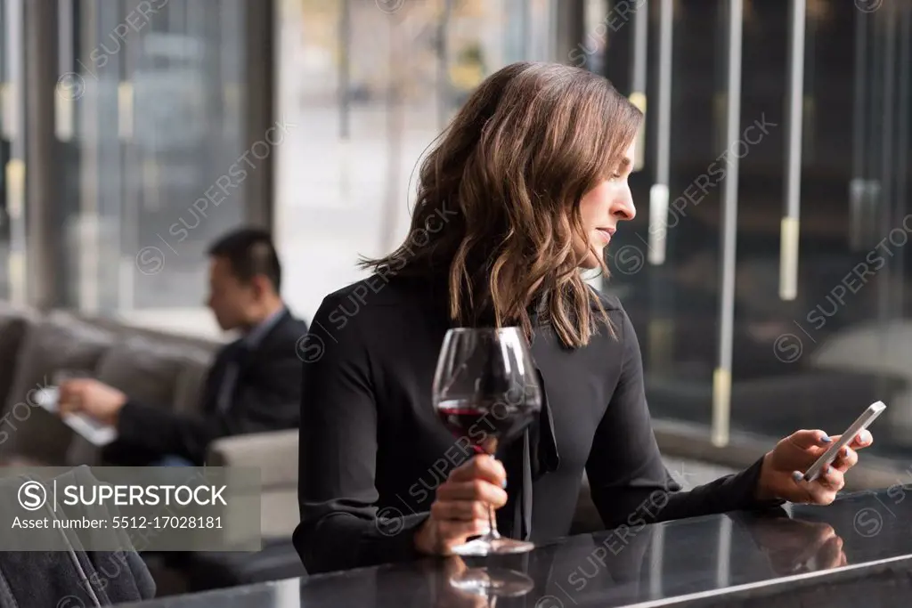 Businesswoman having red wine while using mobile phone in hotel