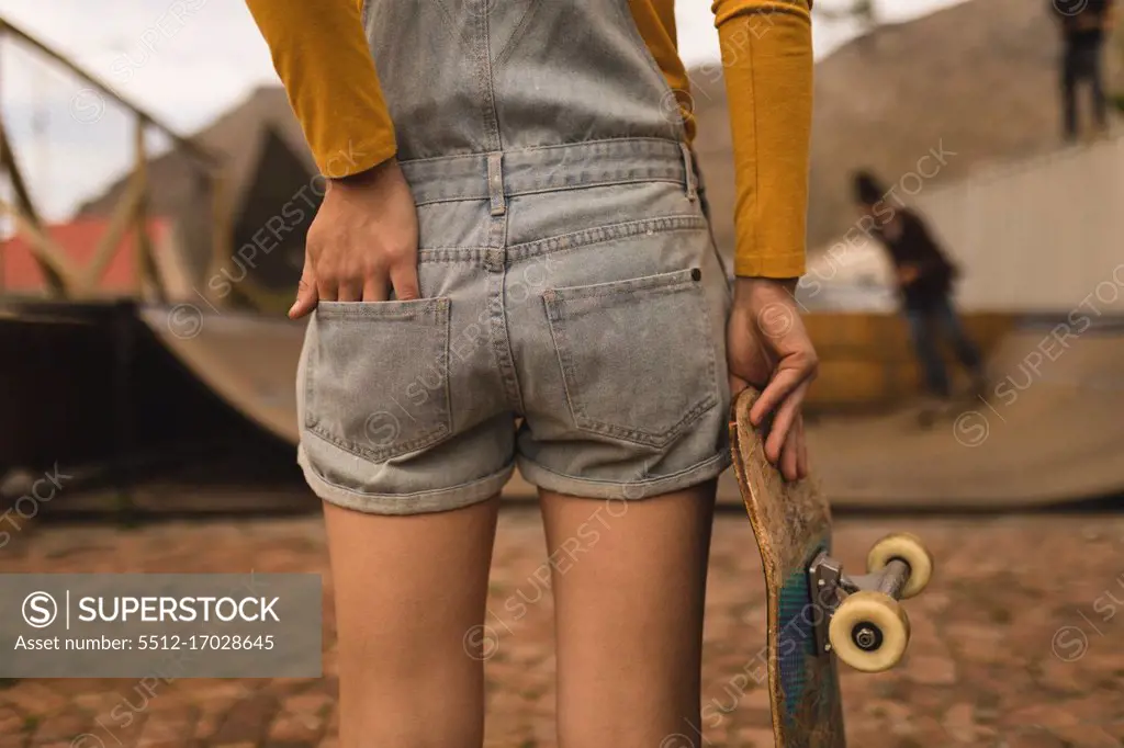 Mid section of female skateboarder standing with skateboard