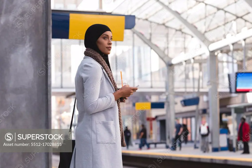 Hijab woman waiting for train while using mobile phone at railway station