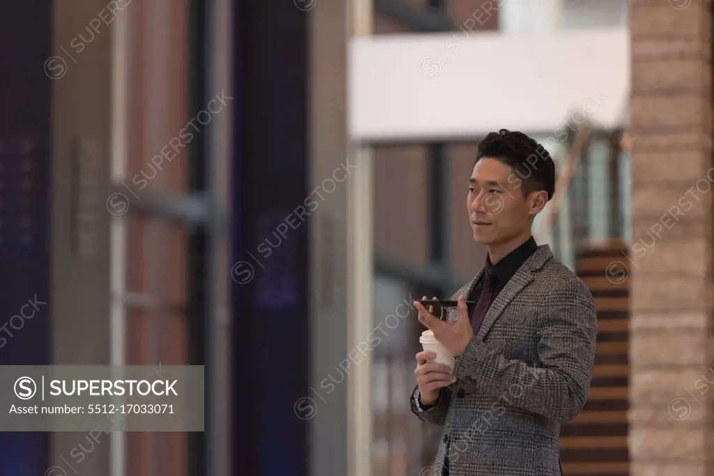 Side view of businessman holding mobile phone while having coffee in the modern office