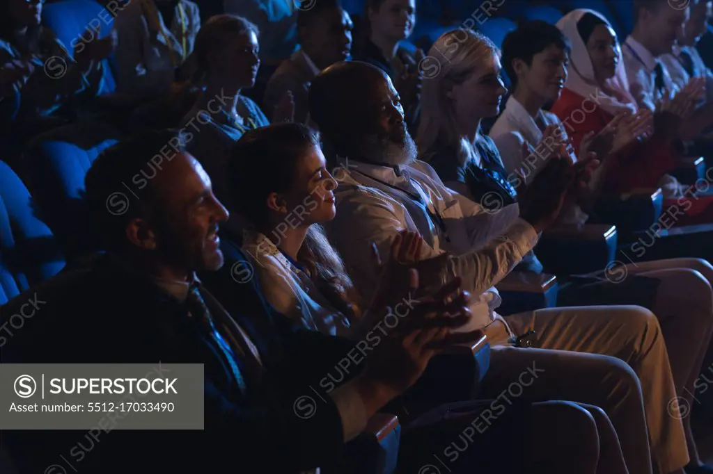 Side view of mixed race business colleagues sitting and watching presentation with audience and clapping hands