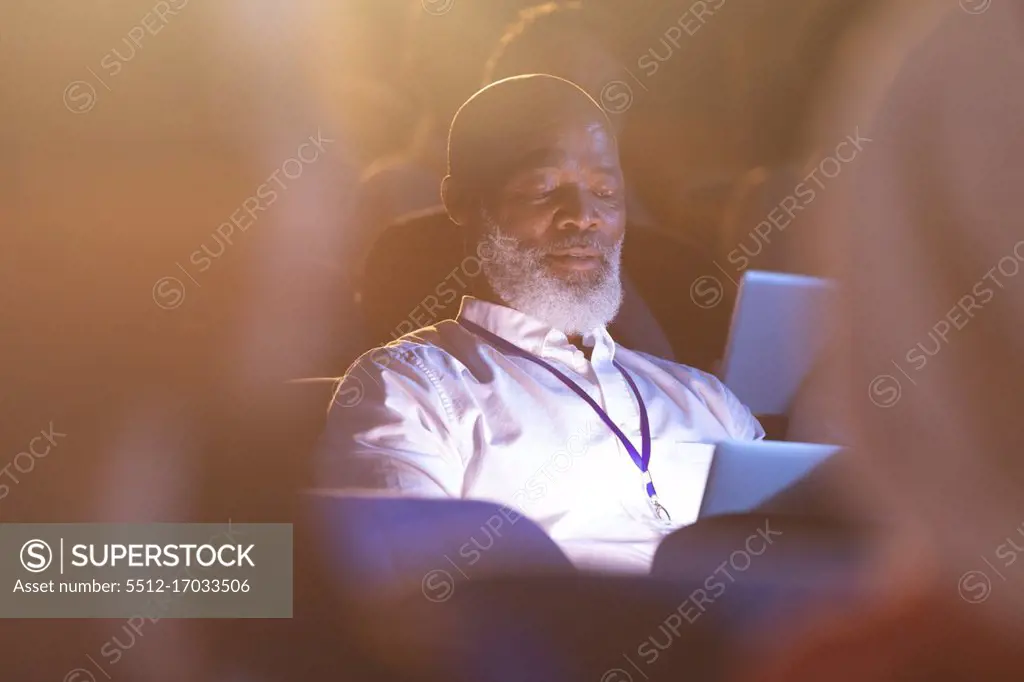 Front view of old African-American businessman looking at digital tablet while sitting in the auditorium 