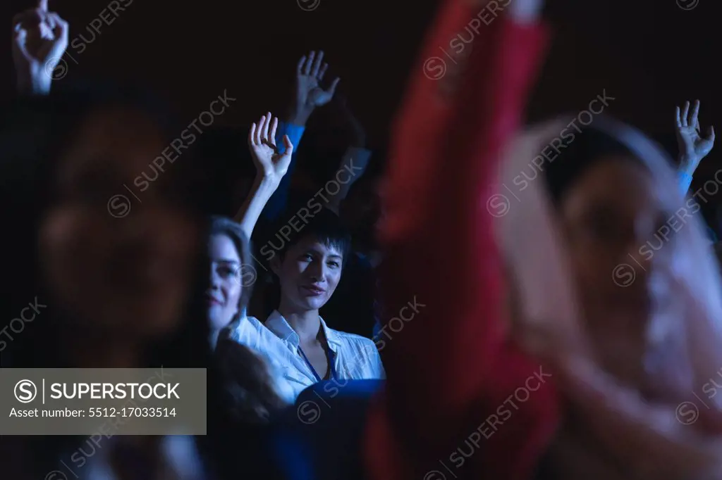 Low angle view of beautiful Asian businesswoman sitting and raising hand while sitting in auditorium