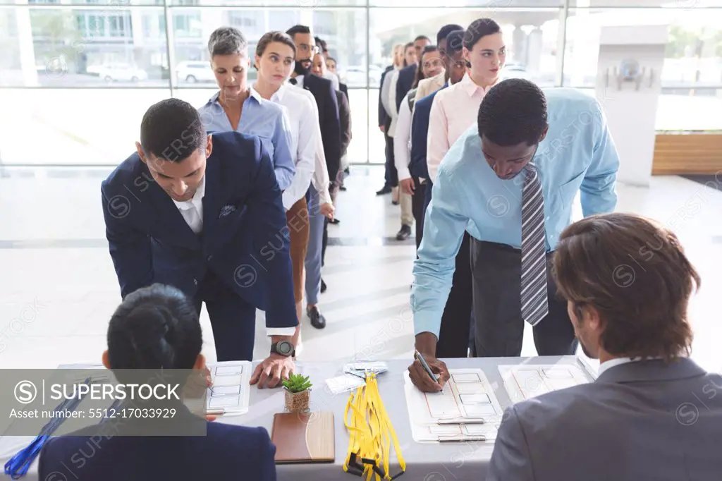 Front view of diverse business people checking in at conference registration table in office lobby