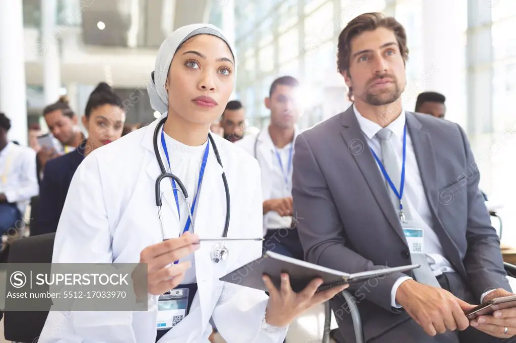 Front view of mixed race female doctor with Caucasian  businessman attending seminar in office. She holding a notebook