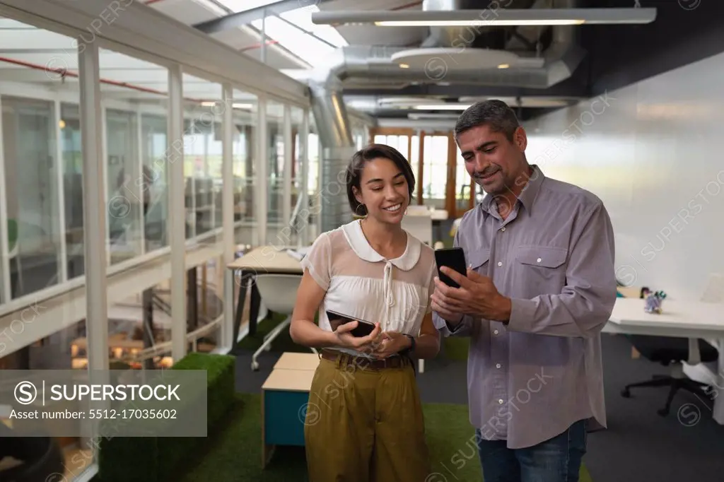 Front view of multi ethnic business people standing in the office while discussing about their mobile phone