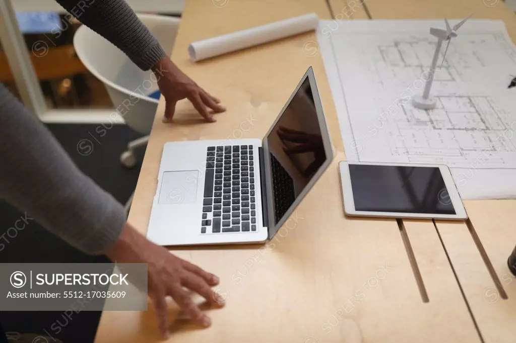 Mid section of a businessman leaning on the desk and looking at his laptop