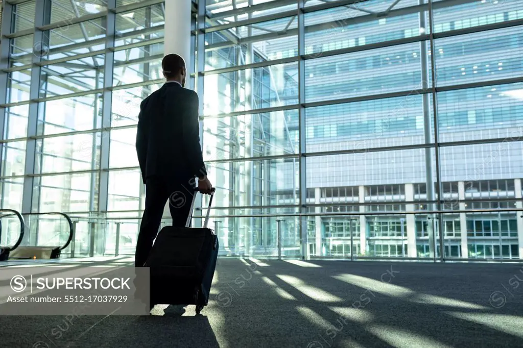 Rear view of businessman with trolley bag standing in the modern office building