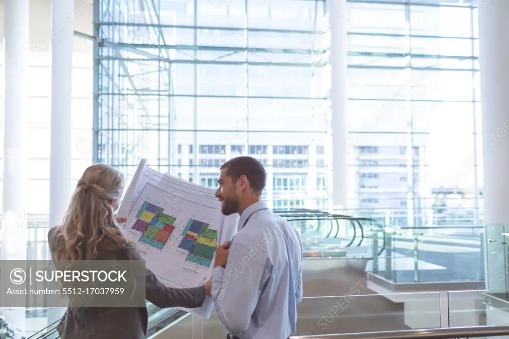 Rear view of business people discussing over blueprint in a modern office building