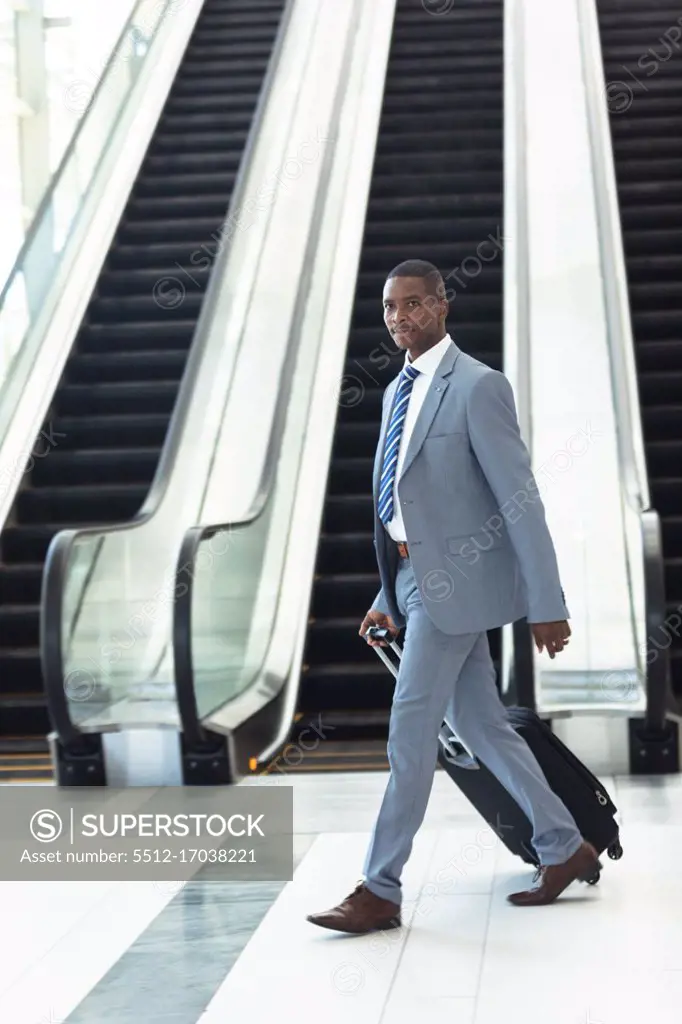 Side view of young African-american executive walking with suitcase in hall