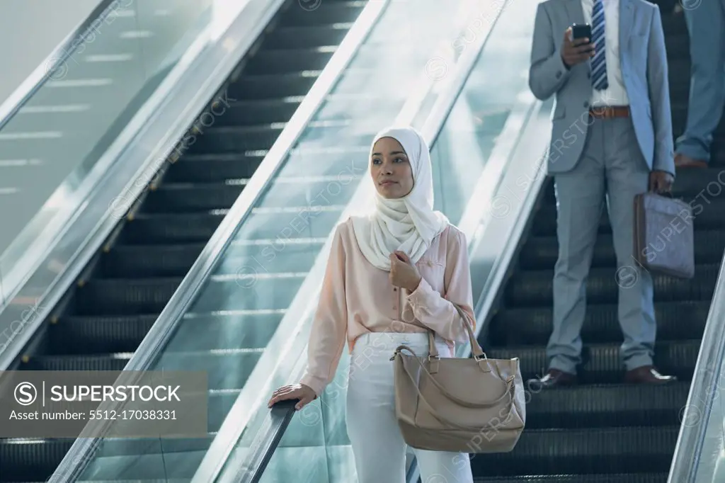 Front view of businesswoman in hijab using escalators in modern office 