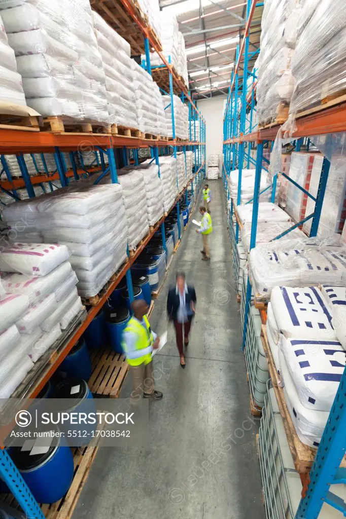 High angle view of diverse warehouse staff checking stocks in aisle in warehouse. They are holding clipboards and writing in it. This is a freight transportation and distribution warehouse. Industrial and industrial workers concept