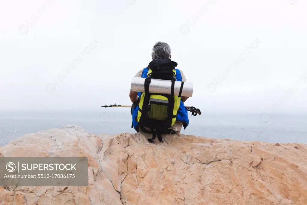 Senior man spending time in nature, walking in the mountains, sitting on a rock and enjoying the view. healthy lifestyle retirement activity.