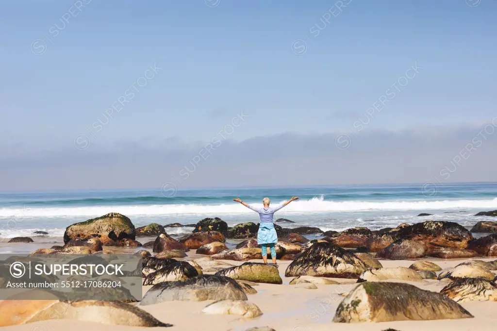 Senior woman spending time in nature, walking on the beach, enjoying the view, raising her arms. healthy lifestyle retirement activity.