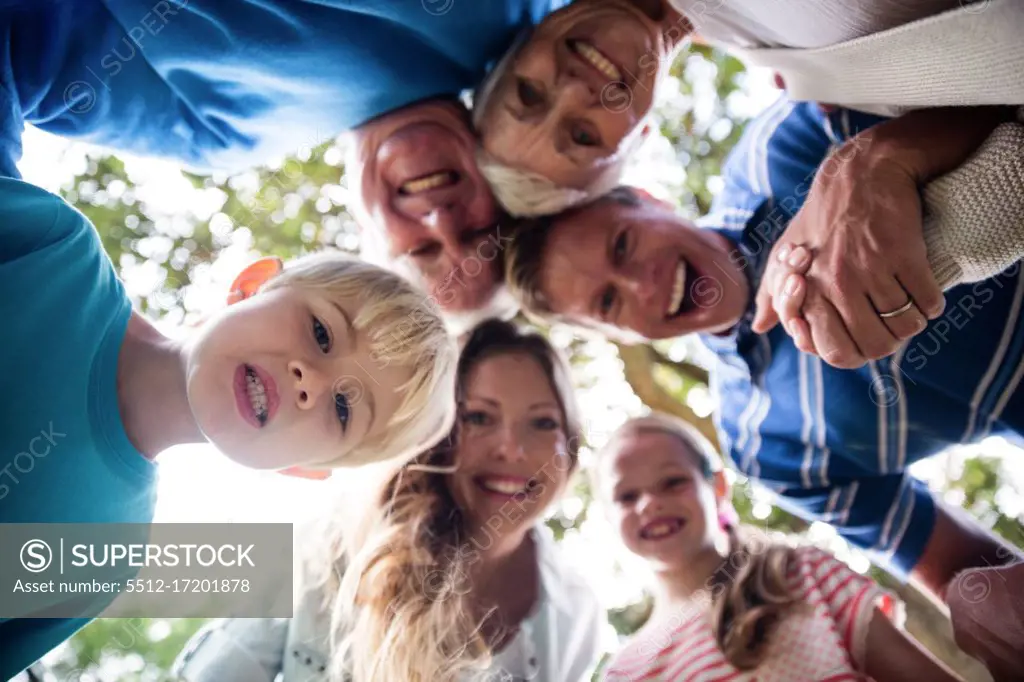 Portrait of happy multi-generation family forming a huddle in park on a sunny day