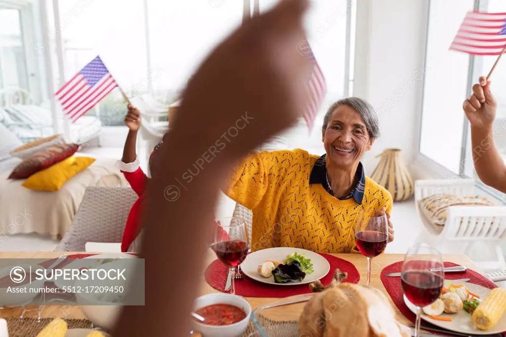 Side view of Multi-generation African American family holding American flag and having celebration on a dining table at home