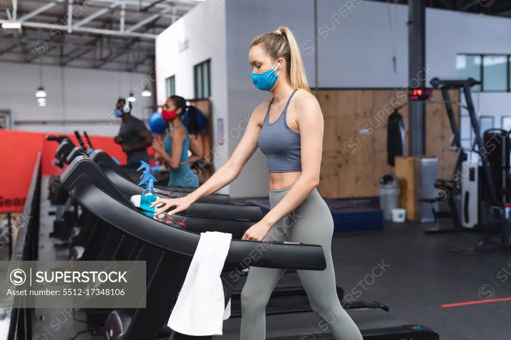 Fit caucasian woman wearing face mask running on treadmill doing