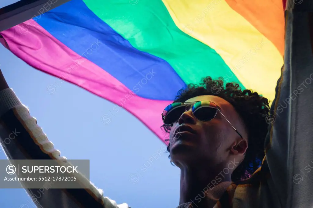 Mixed race man standing on rooftop holding rainbow flag. gender fluid lgbt identity racial equality concept.