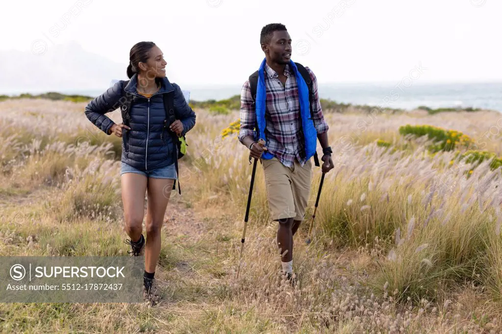 Fit african american couple wearing backpacks nordic walking on coast. healthy lifestyle, exercising in nature.