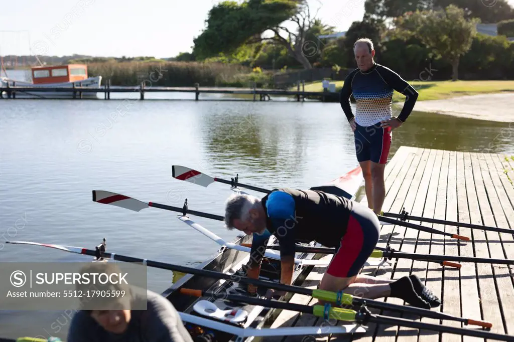 Senior caucasian rowing team attaching oars to the boat near the wooden dock. retirement sports and active senior lifestyle.