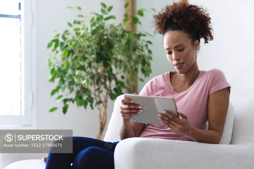 Mixed race woman using tablet in living room. staying at home in self isolation during quarantine lockdown.