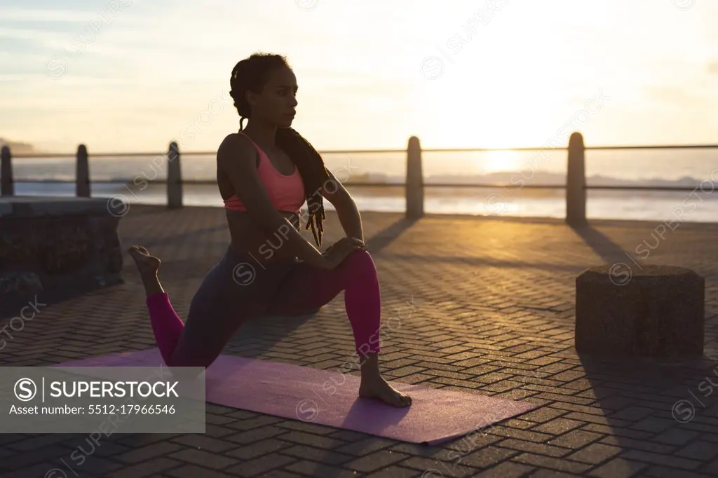 African american woman exercising on promenade by the sea doing yoga. fitness healthy outdoor lifestyle.