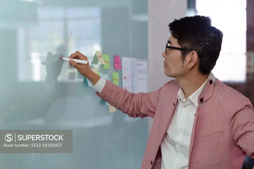 Stylish asian businessman writing notes on glass wall. business person at work in modern office.