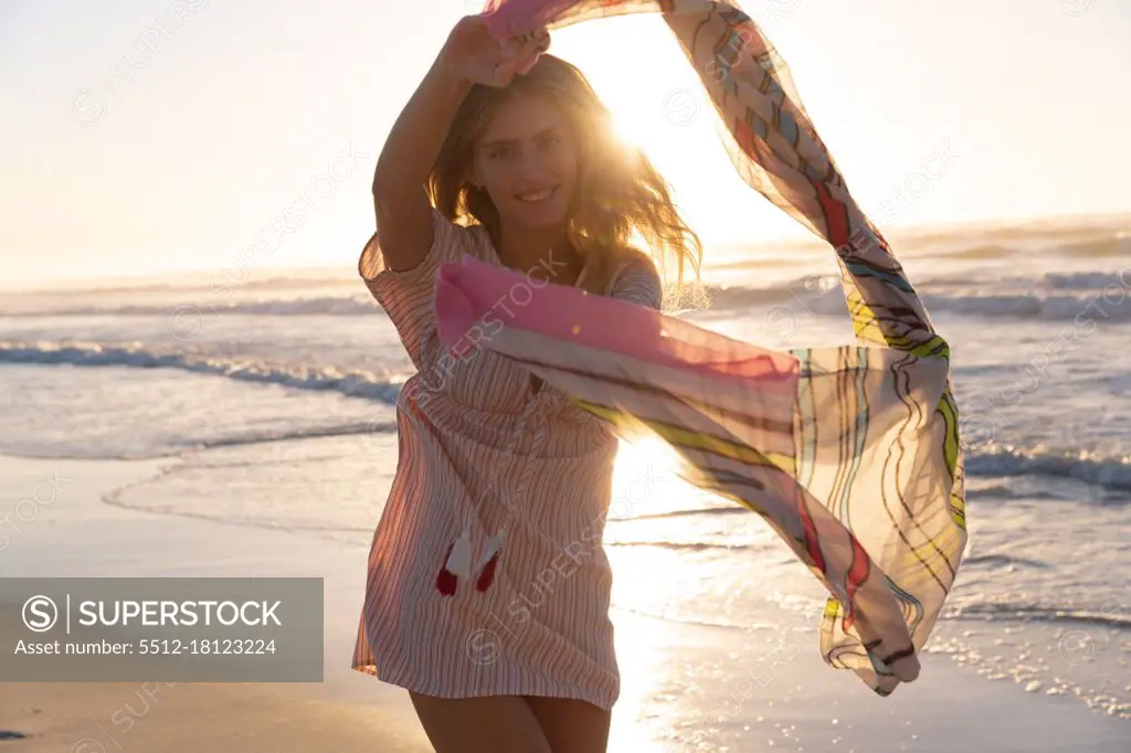 Portrait of caucasian woman holding scarf smiling while standing at the beach. summer beach holiday concept.