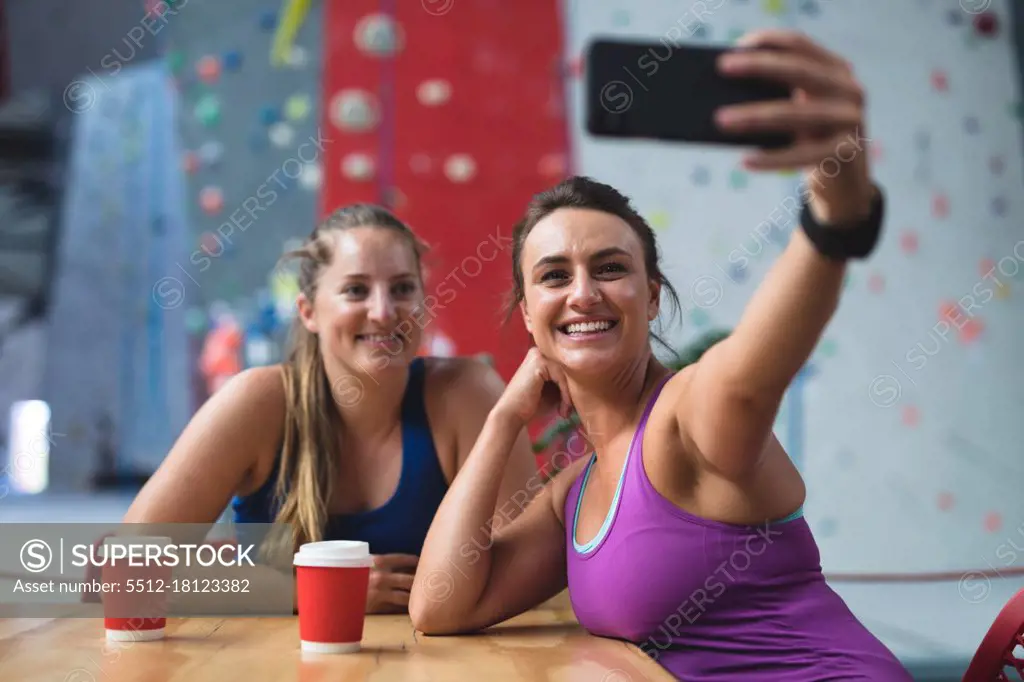 Two happy caucasian women taking selfie with smartphone in cafe at indoor climbing wall. fitness and leisure time at gym.