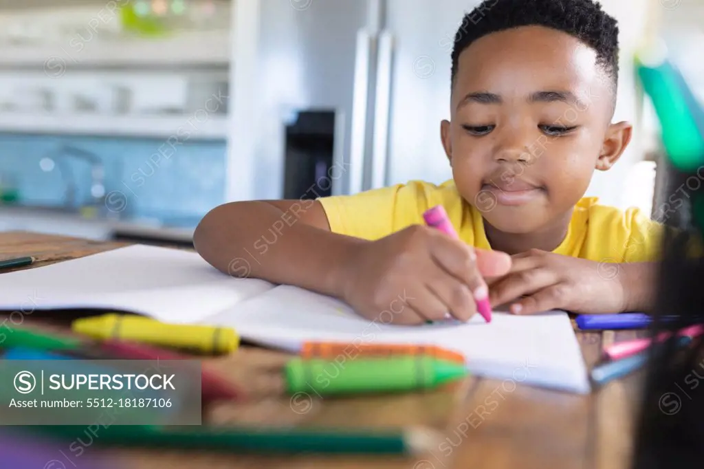 African american boy sitting at table, writing in notebook. at home in isolation during quarantine lockdown.