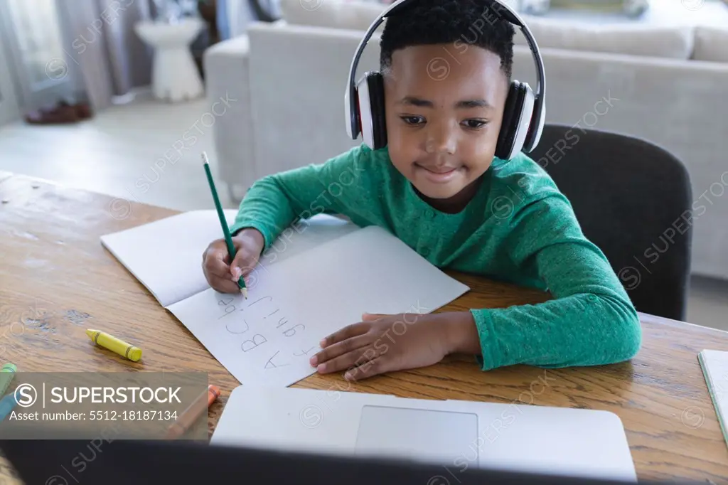 African american boy in online school class, using headphones and laptop. at home in isolation during quarantine lockdown.