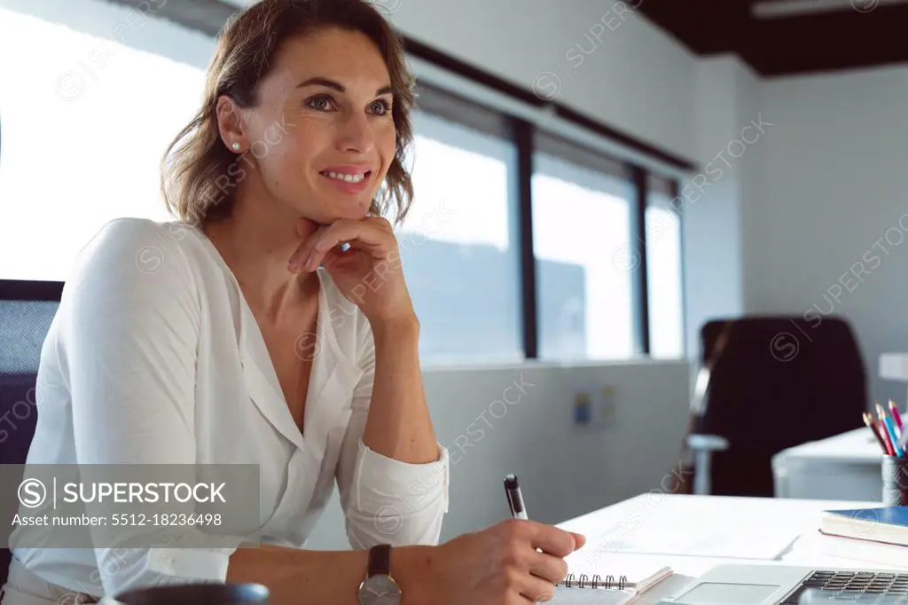 Smiling caucasian businesswoman sitting at desk, making notes at work. independent creative business at a modern office.