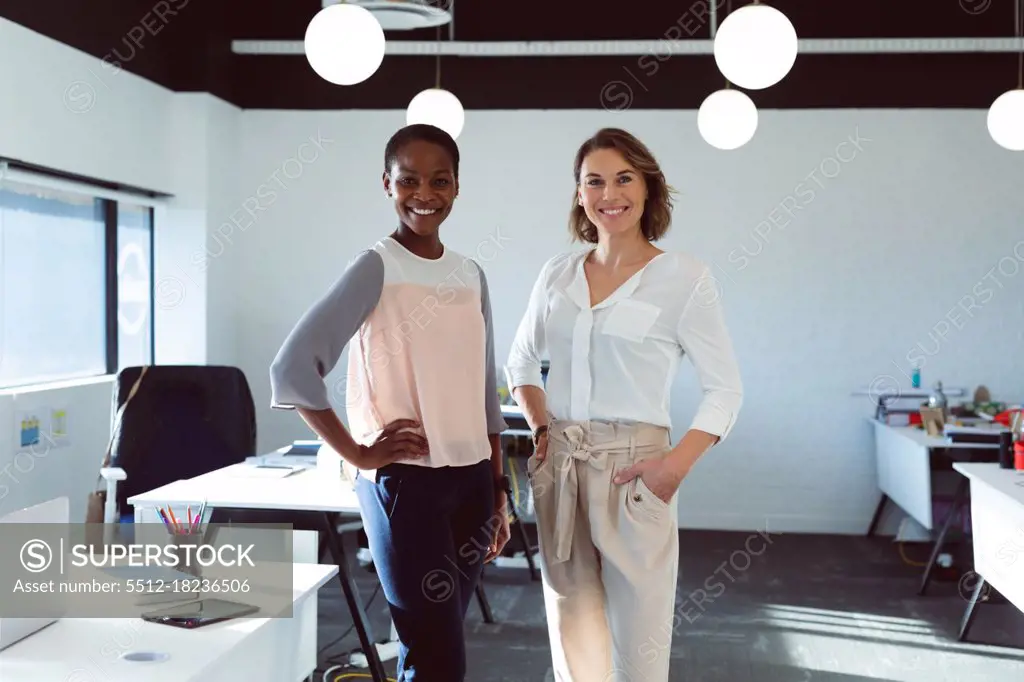 Two smiling diverse businesswomen standing and looking at camera at work. creative business at a modern office.