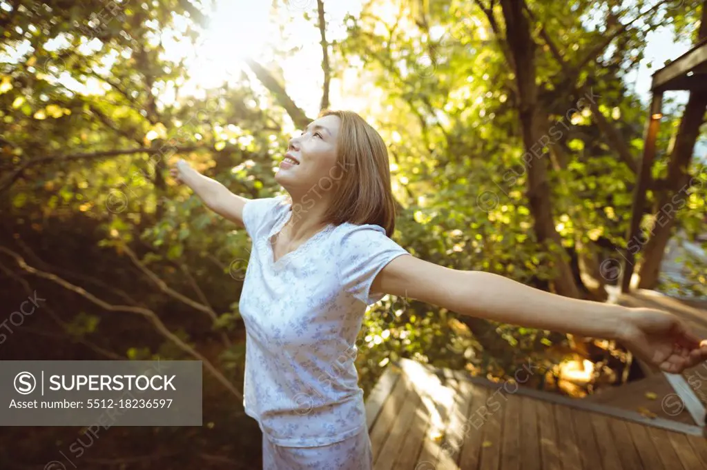 Smiling asian woman in pyjamas with her arms outstretched in garden. at home in isolation during quarantine lockdown.