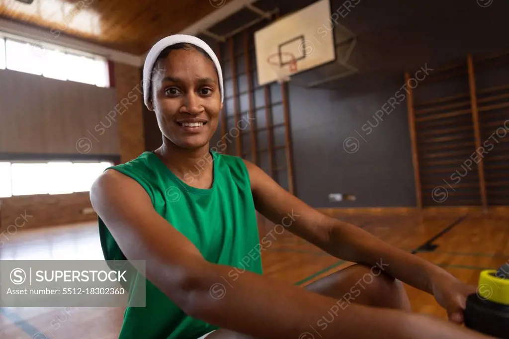 Portrait of mixed race female basketball player with bottle of water and smiling. basketball, sports training at an indoor court.