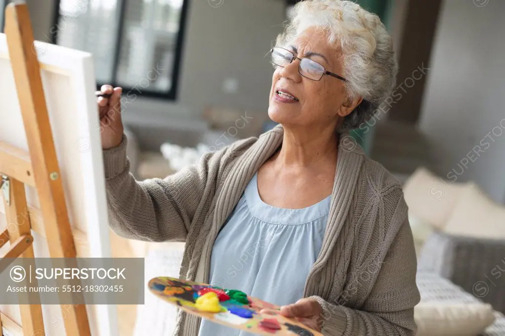 Mixed race senior woman painting on canvas in living room. staying at home in isolation during quarantine lockdown.