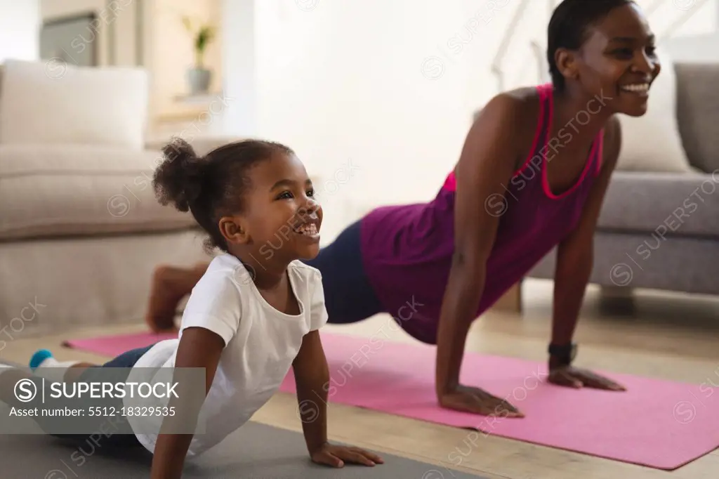 Smiling african american mother and daughter practicing yoga, lying on mats stretching. family spending time together at home.