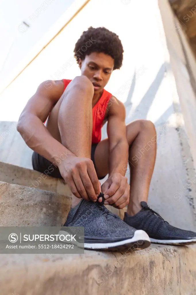 Fit african american man exercising in city tying shoes. fitness and active urban outdoor lifestyle.