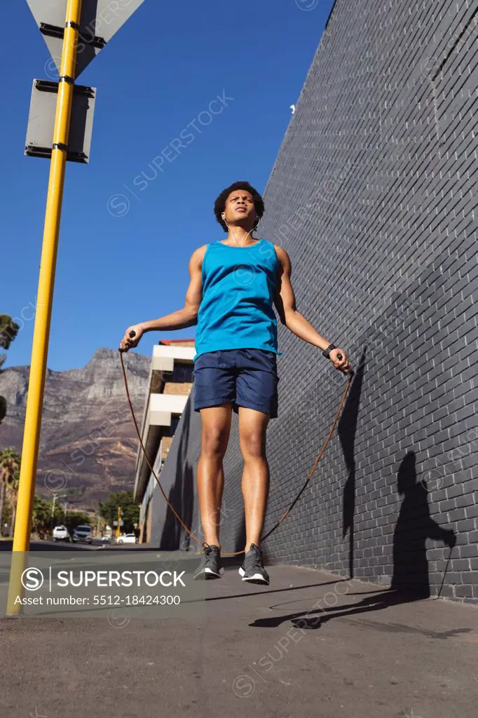 Fit african american man exercising in city jumping with skipping rope in the street. fitness and active urban outdoor lifestyle.