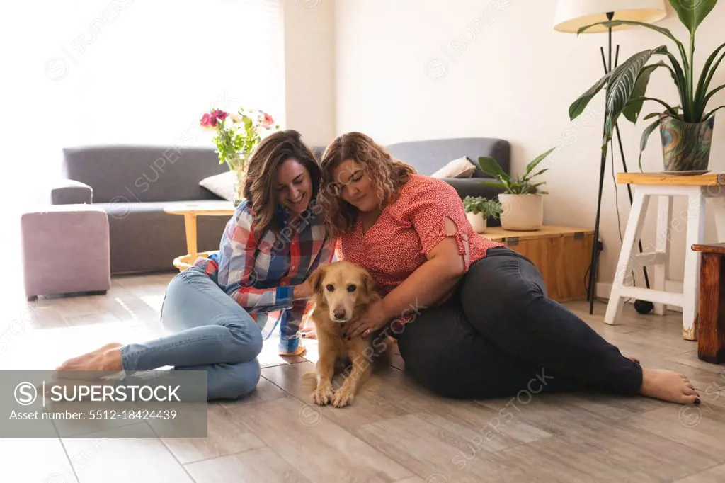 Happy lesbian couple sitting on floor embracing and smiling with their dog. domestic lifestyle, spending free time at home.