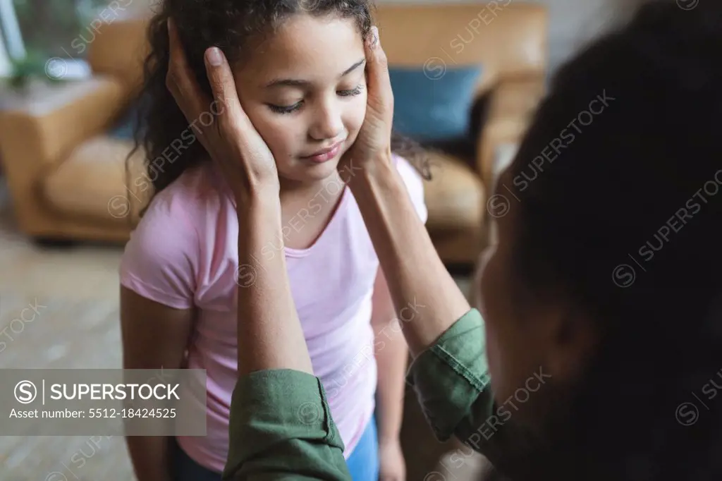 Mixed race mother sitting on sofa and touching her daughter's head. domestic lifestyle and spending quality time at home.