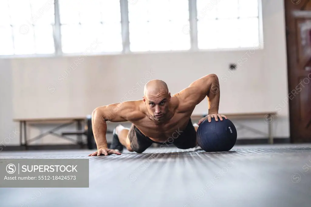 Strong caucasian man exercising at gym, doing push-ups using ball. strength and fitness cross training for boxing.